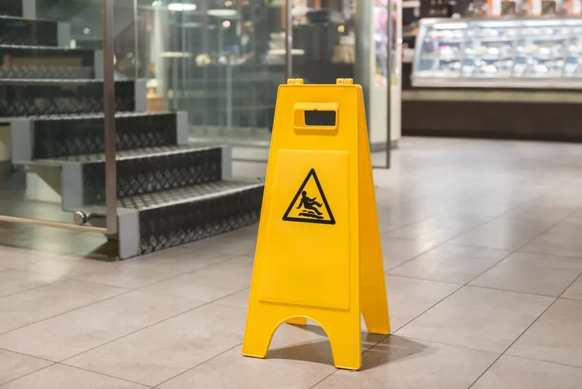 Warnschild "Vorsicht rutschig" steht auf nassen Fliesen im Einkaufszentrum