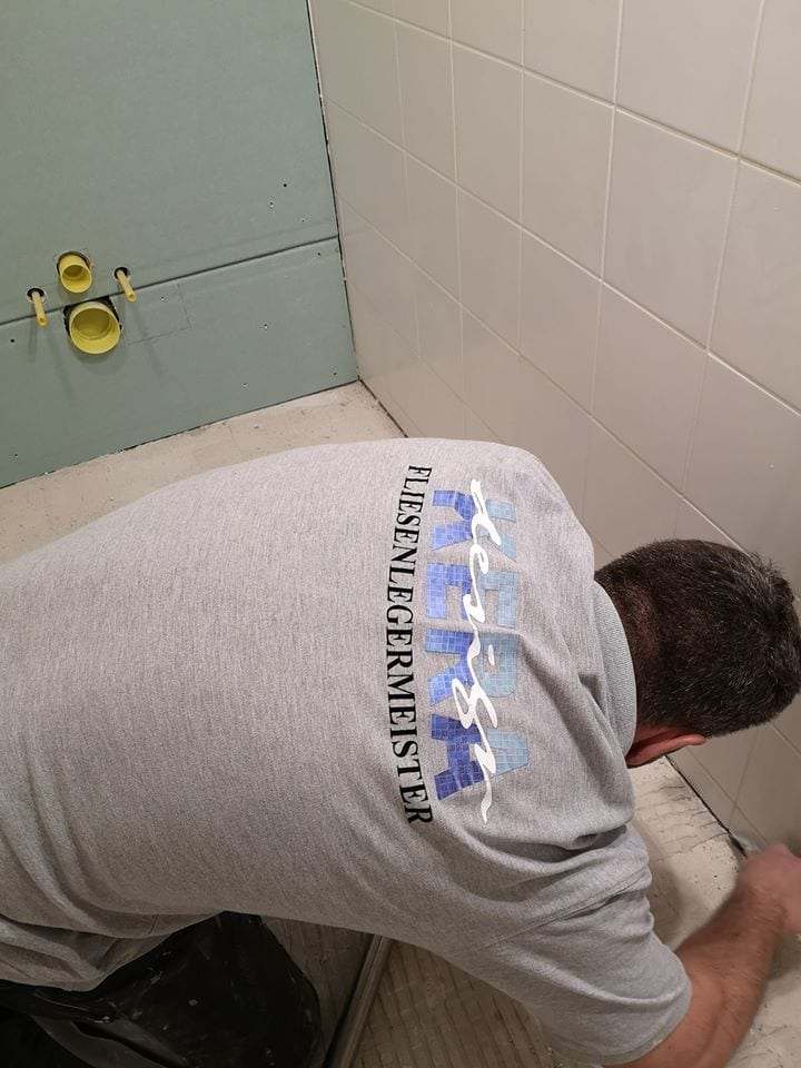 Fliesenleger im Meisterbetrieb-Shirt beim Verlegen an einer Wand