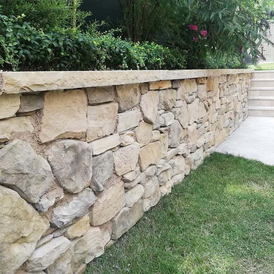 Gartenmauer aus Naturstein neben einem gepflasterten Weg