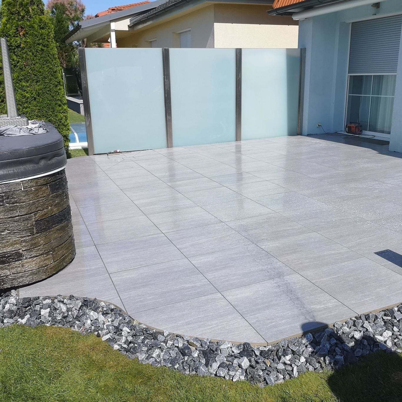 Terrasse mit hellen grossformatigen Bodenplatten und Sichtschutz aus Glas