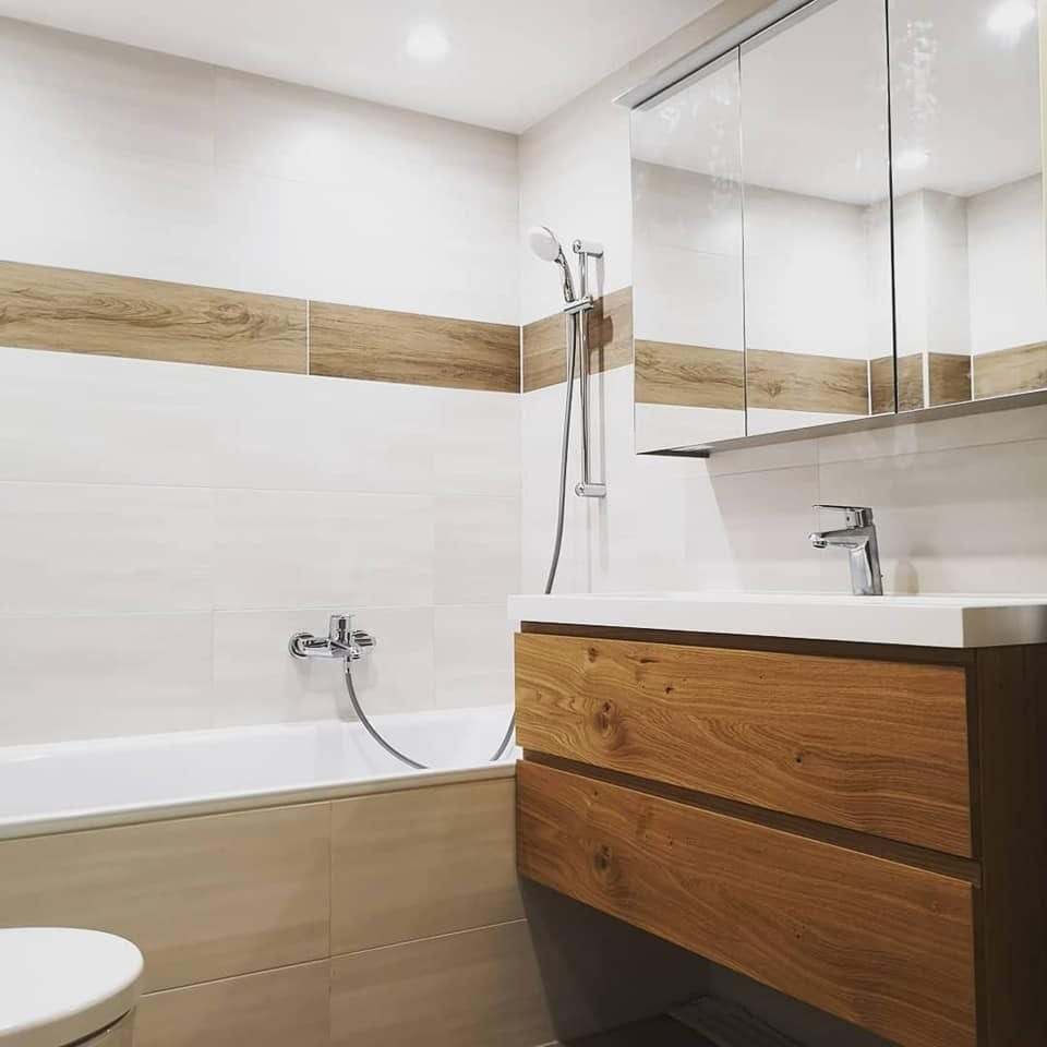 Badewanne mit Holzverkleidung vor hellen Wandfliesen