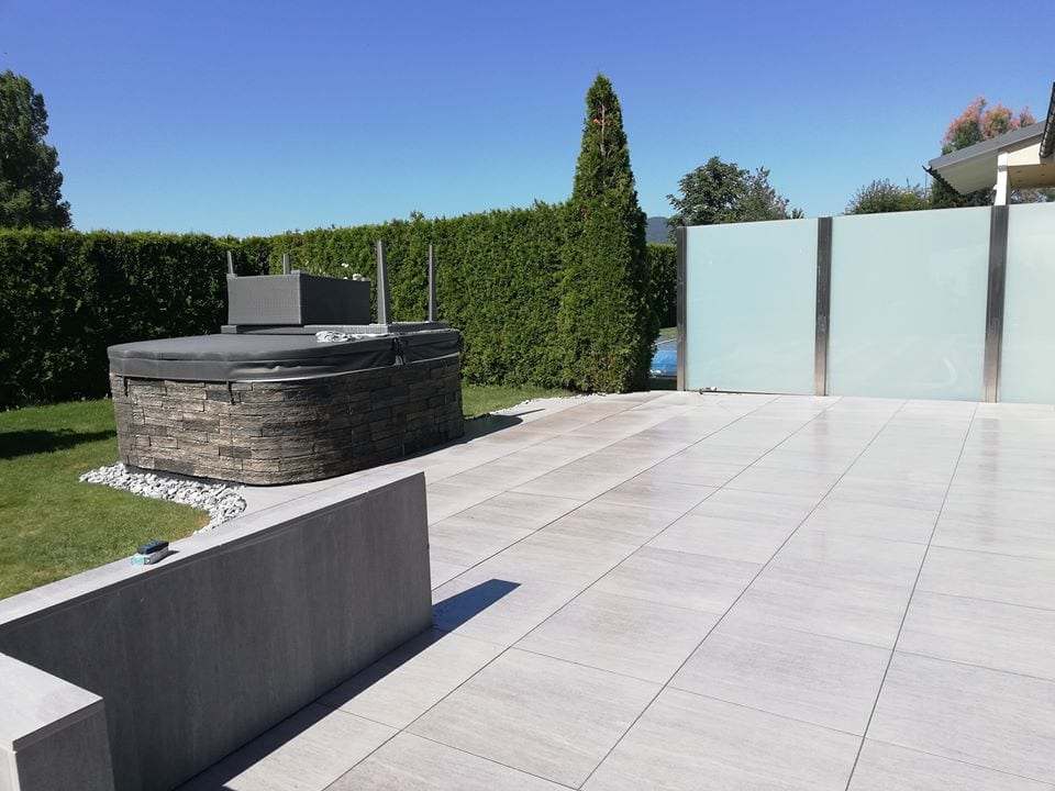 Terrasse mit hellen Platten, Sichtschutz aus Glas und Hochbeet