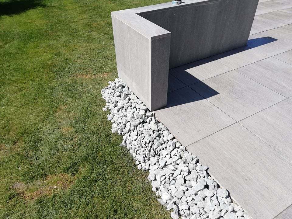Terrassenkante mit hellen Platten, Ziersteinen und Rasen